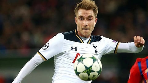 Christian Eriksen in a white Tottenham Hotspur jersey focuses intently as he kicks a ball mid-air during a match.