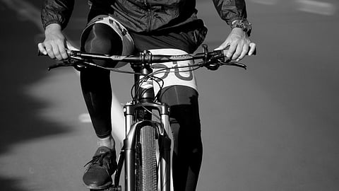 Black and white image of a cyclist riding on a road. 