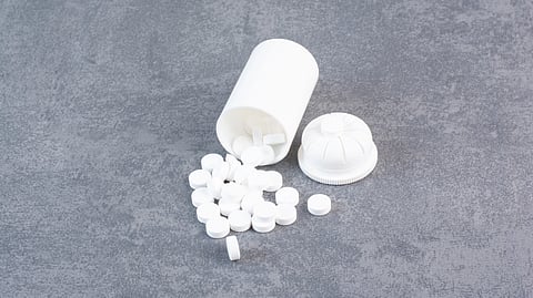White pills spill from a tipped-over bottle on a gray textured surface.