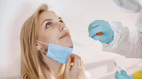 A woman wearing a lowered face mask receives a nasal swab test from a healthcare worker in protective gear.