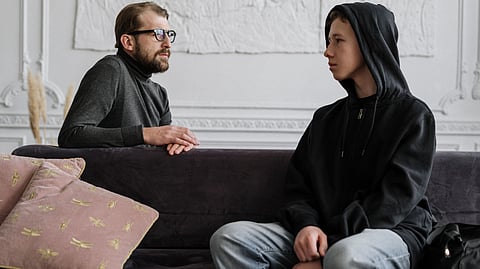 A man and a young boy sit together on a couch, engaged in a conversation and sharing a moment of connection.