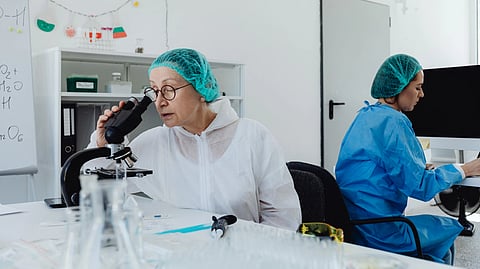 Two women in lab coats examining a microscope in a laboratory setting.