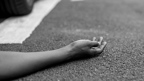 A person lying on the road beside a car.