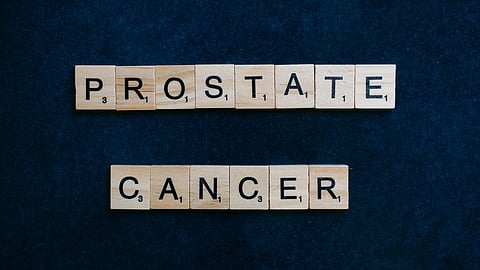 Wooden Scrabble tiles spell out "Prostate Cancer" on a dark blue background.