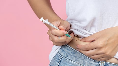 A person injects medication into their abdomen with a syringe.