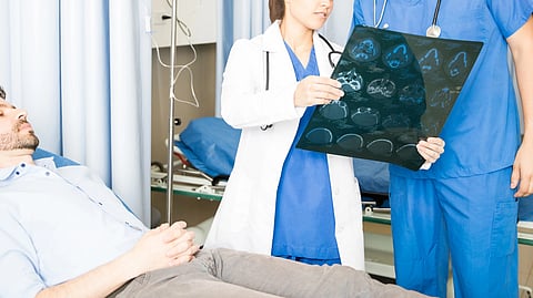 A doctor and nurse review an MRI scan beside a patient in a hospital room.
