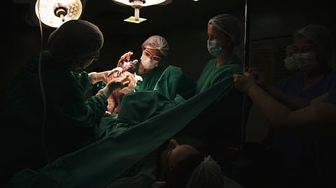 Doctors in masks and scrubs deliver a newborn in dimly lit operating room.