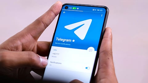 A person holds a smartphone displaying the Telegram app.
