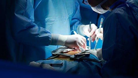 Two surgeons, a man and a woman, perform an operation in a dimly lit operating room.