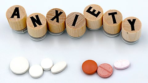 The word “ANXIETY” is spelled with wooden letters above a few pills.