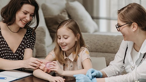 An adult woman and a girl sit with a doctor who is observing a small medical device.