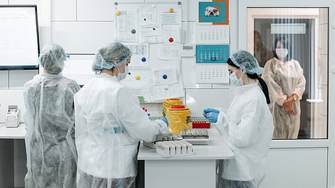 Three researchers in lab coats discuss and work together around a table.