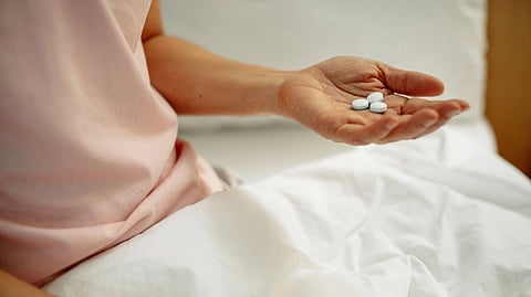 A person sitting on a bed, holding a pill in their hand.