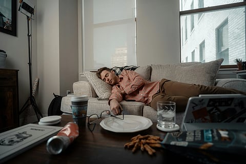 Man asleep on couch after a heavy meal with empty plate on table in front