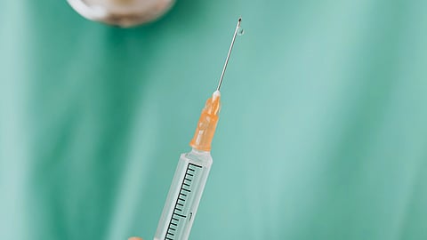 A close-up of a hand holding a syringe against a green medical scrub background.