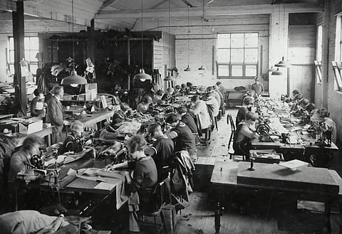 Black and white historical photograph of workers at sewing machines in an early 20th century factory workshop