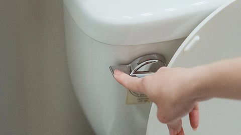 A hand presses a toilet flush handle on a white ceramic toilet.