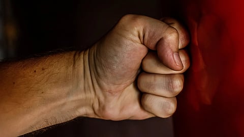 A close-up side view of a person's clenched fist pressing firmly against a smooth, vertical red surface. 