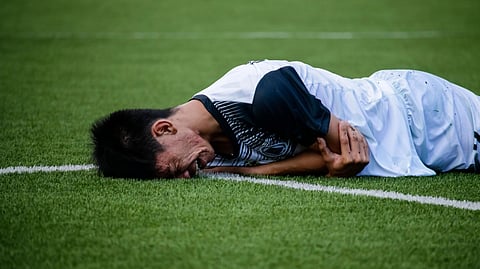 An injured athlete lies on a turf field holding their arm in pain.