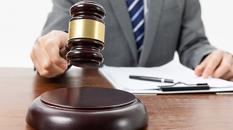 A person in a suit holds a gavel above a desk, with a clipboard and pen nearby.