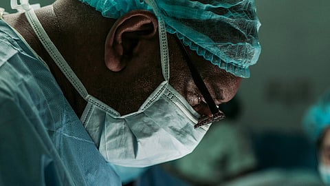 Surgeon in scrubs, cap, and mask focused during a procedure