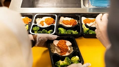 Black meal boxes containing broccoli, rice, some form of protein and a red sauce as a part of medically tailored meal planning program