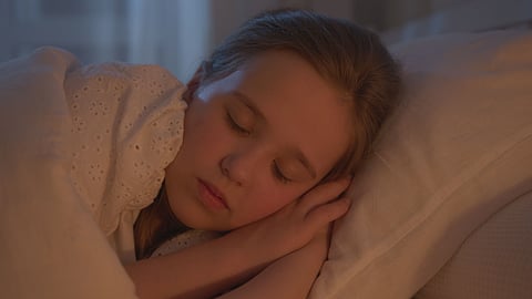 A young girl sleeps peacefully on a pillow under warm, soft lighting, creating a calm and cozy mood.