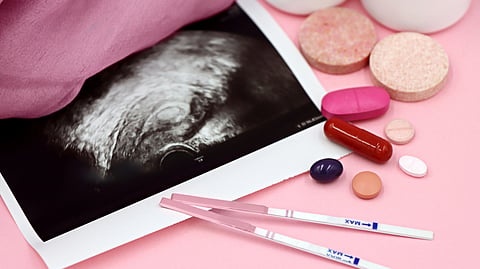 Ultrasound image on a pink surface with two pregnancy test strips, various pills, and round tablets.