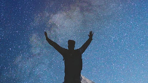 Silhouette of a person with raised arms against a starry night sky.