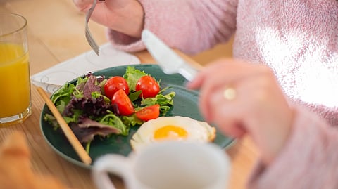 A woman enjoying a meal consisting of a salad and a boiled egg on a plate.