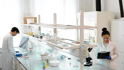 Two individuals in lab coats collaborating on a computer in a laboratory setting.