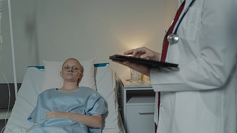 A woman lies in a hospital bed while a doctor examines her, discussing her condition.