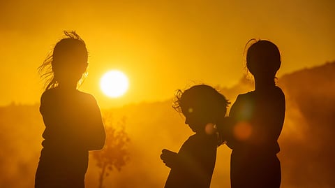 Three people are silhouetted against a vibrant orange and yellow sunset.