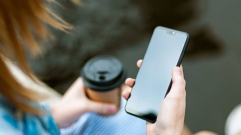 A person holds a smartphone in one hand and a coffee cup in the other.