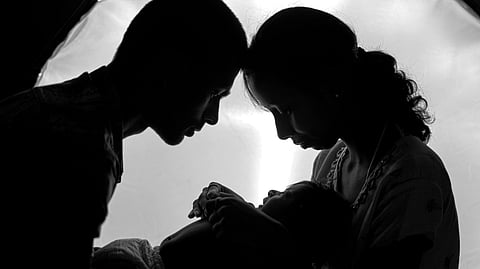 A black and white silhouette of parents looking at their baby.