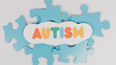 Blue puzzle pieces with a cloud cutout reading “AUTISM” in colorful letters.