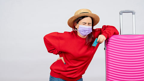 A traveler with a suitcase holds their lower back in pain while standing.