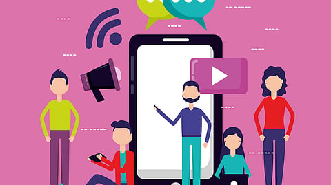 Vibrant pink illustration of social media: big smartphone with presenter, five diverse people around it with laptops and tablets, floating video, chat, WiFi, and megaphone icons.