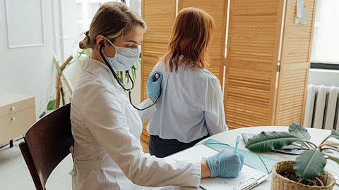 A doctor sits at a desk holding a stethoscope.