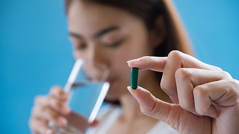 A woman holds a pill with a glass of water nearby.
