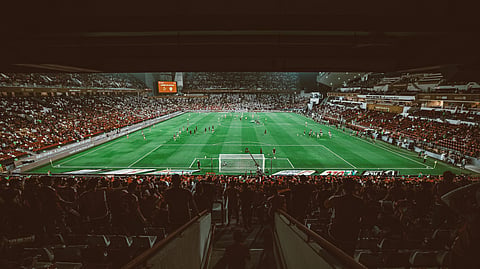 An expansive, high-angle view from the stands of a packed soccer stadium at night. 