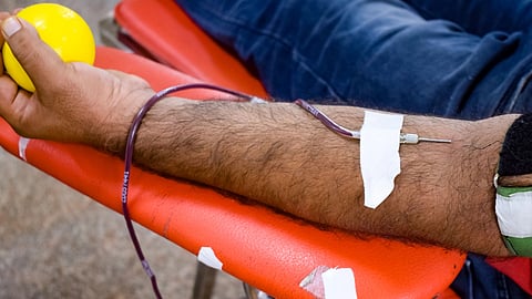 A person donates blood while squeezing a yellow stress ball.