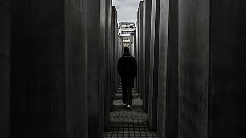 A person walks on a narrow path between tall concrete pillars under a cloudy sky.
