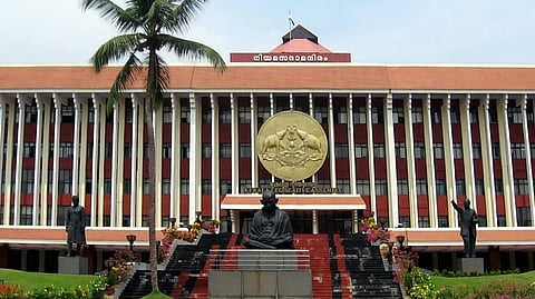 The Kerala Legislative Assembly building with white pillars, an orange roof, and a statue of Mahatma Gandhi in front.