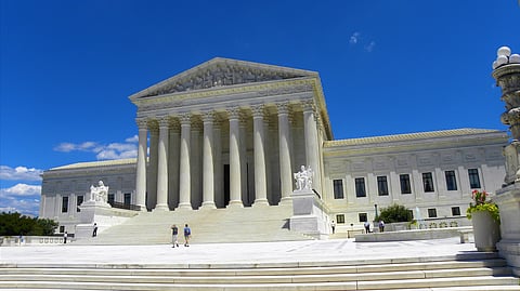 Low-angle wide shot of the U.S. Supreme Court building under a clear blue sky with light clouds.