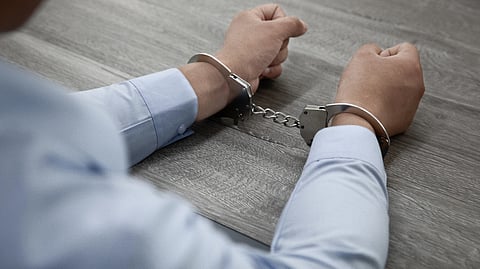 A person in a light blue shirt with handcuffs resting on a table.