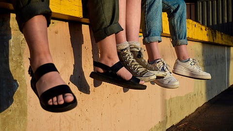 Three people sit together on a yellow ledge with their legs hanging down.