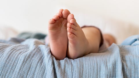 A close-up shot of a baby's tiny feet resting on a light blue muslin blanket.