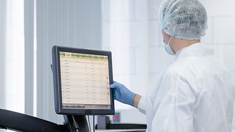 Laboratory professional in PPE operating a clinical chemistry analyzer with results on screen
