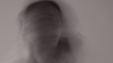 A blurry black-and-white long-exposure photo of a person with a ghostly, moving effect.